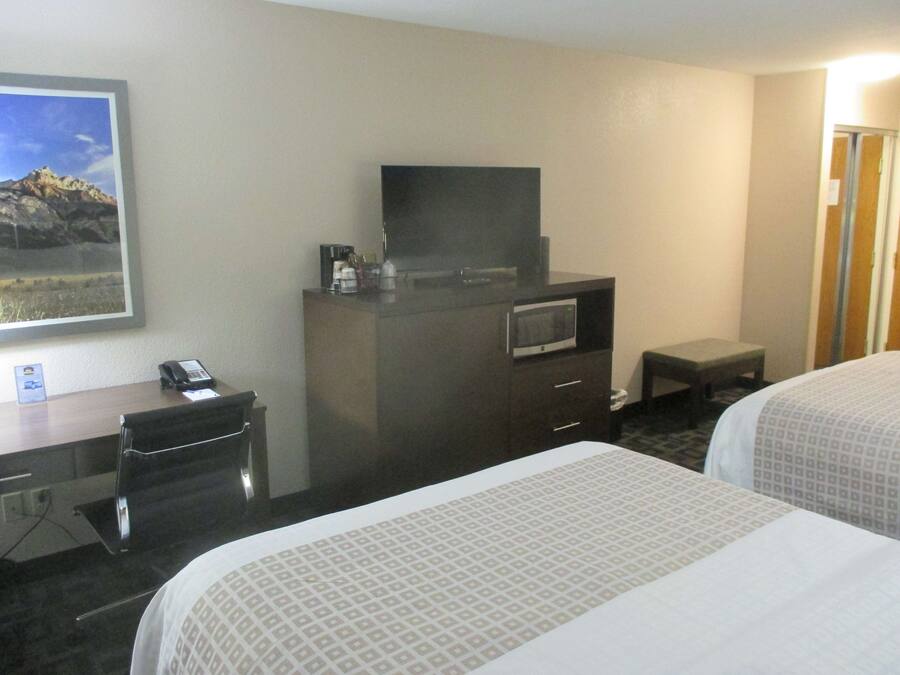 A hotel room with a bed, a desk with a telephone, a television on a dresser, and a small table.