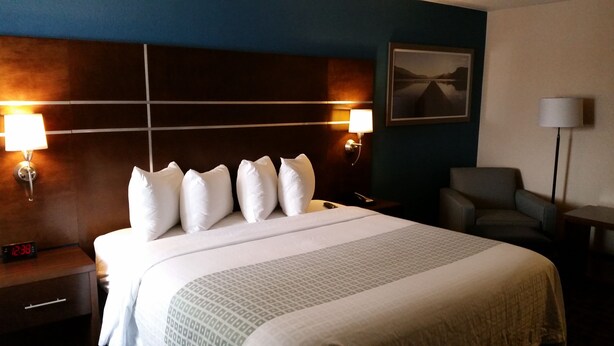 A hotel room with a large bed, two bedside lamps, a nightstand with a clock, a chair, and a framed picture on the wall.