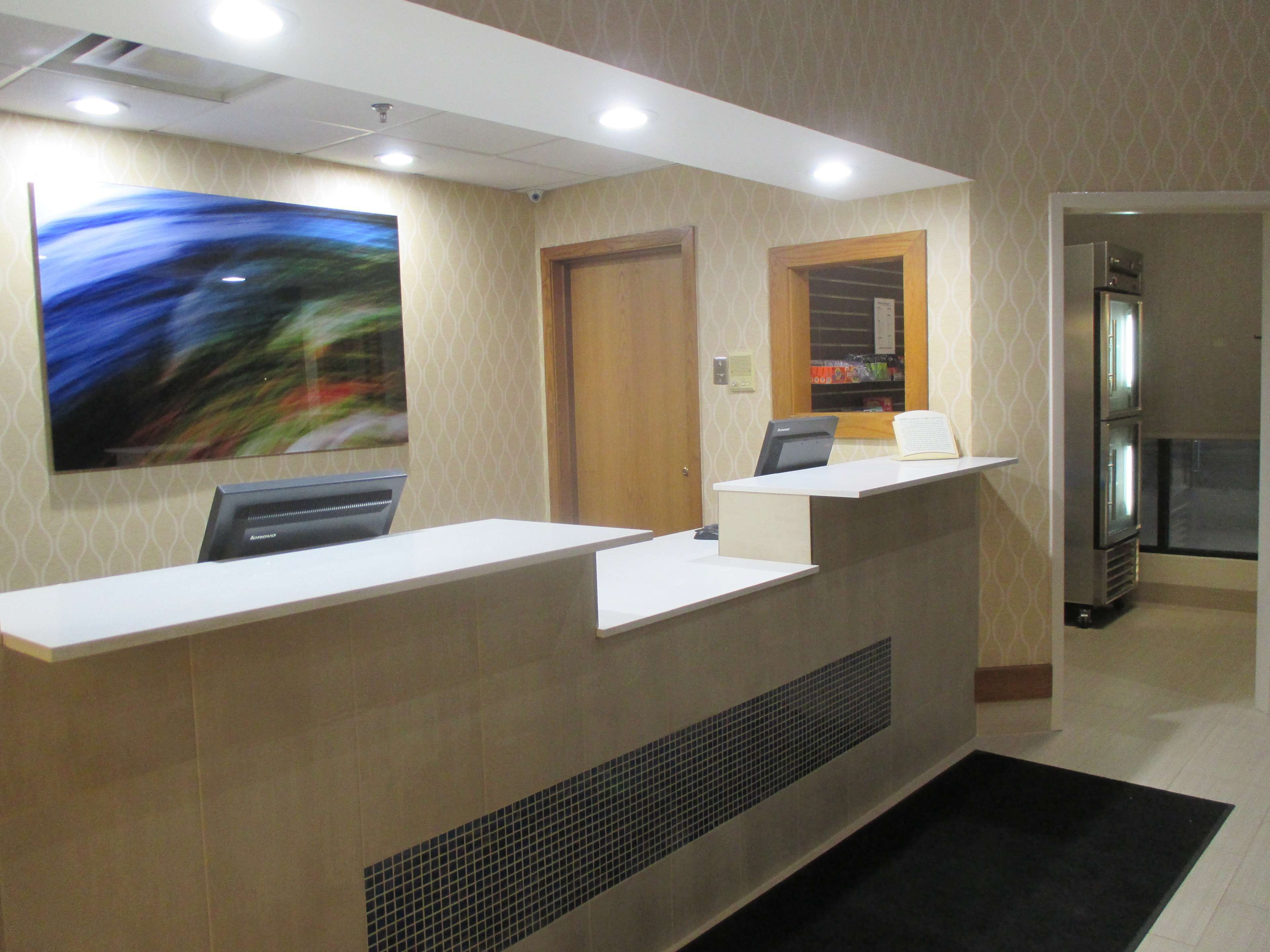A reception desk with a computer, a large abstract painting, a door, and a refrigerator in the background.