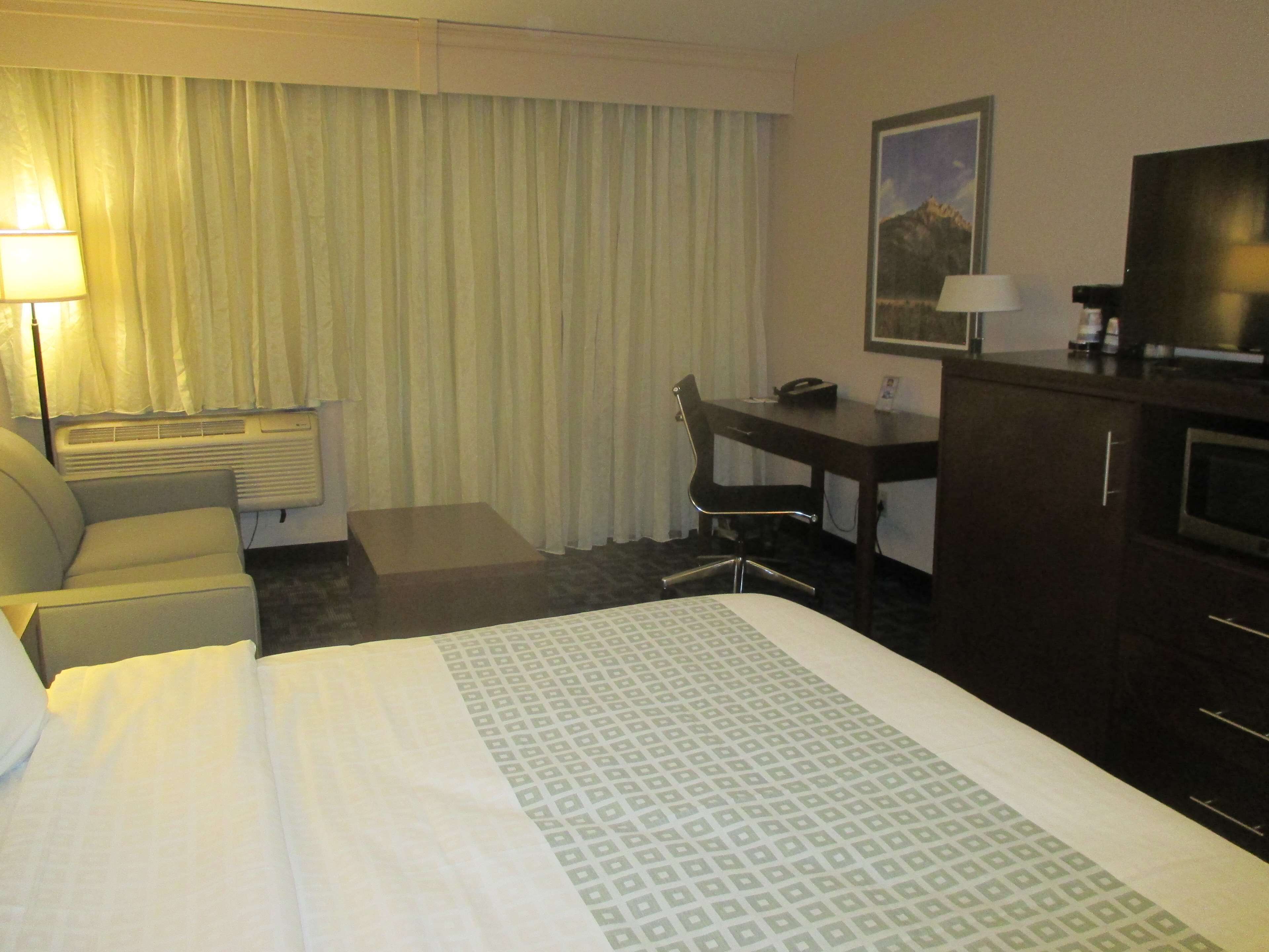 A hotel room with a bed, a desk, a chair, a TV, and a window with curtains.