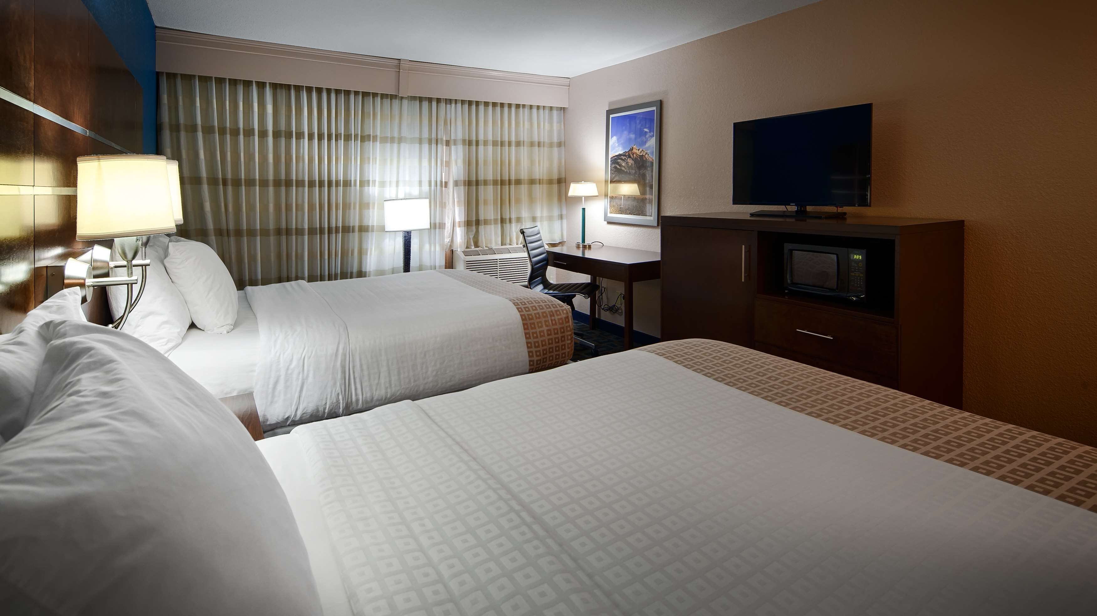 A hotel room with two beds, a desk, a television, and a window with curtains.