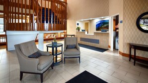 A lobby with a reception desk, seating area with two chairs and a small table, and a decorative wooden partition.