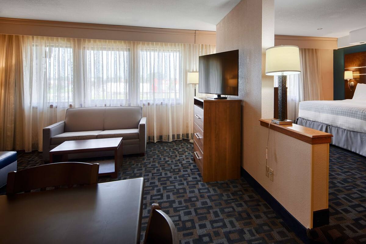 A hotel room with a sofa, a desk, a bed, and a TV.