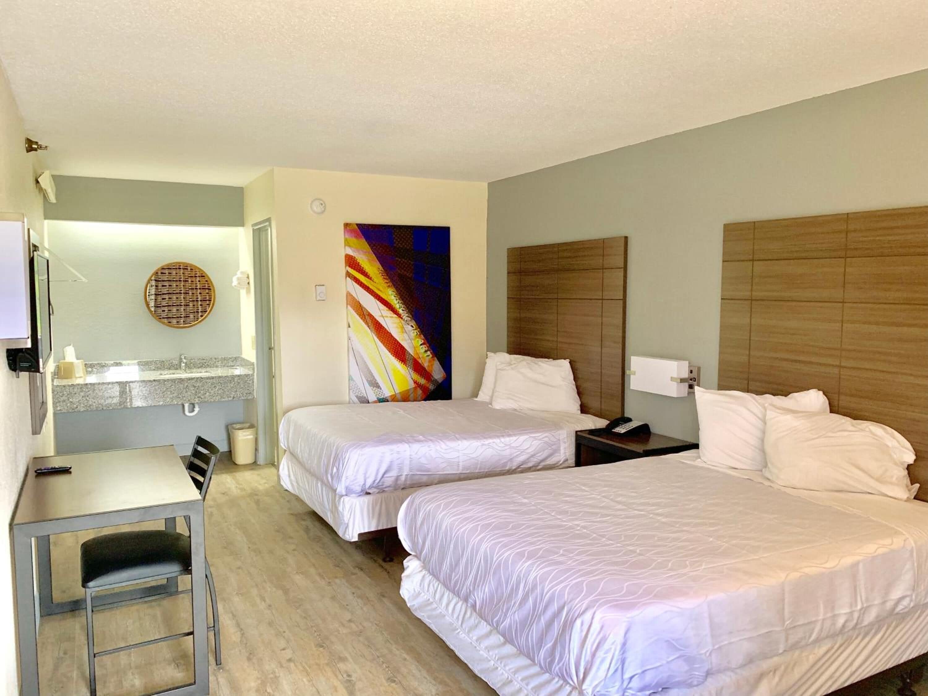 Quarto de hotel com duas camas, uma mesa e um banheiro.