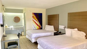 Quarto de hotel com duas camas, uma mesa e um banheiro.