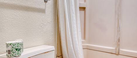 A bathroom with a toilet, a shower curtain, and a towel hanging on the wall.