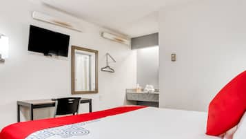 Een hotelkamer met een bed, een bureau, een stoel, een televisie, een spiegel en een badkamer die door een open deur zichtbaar is.