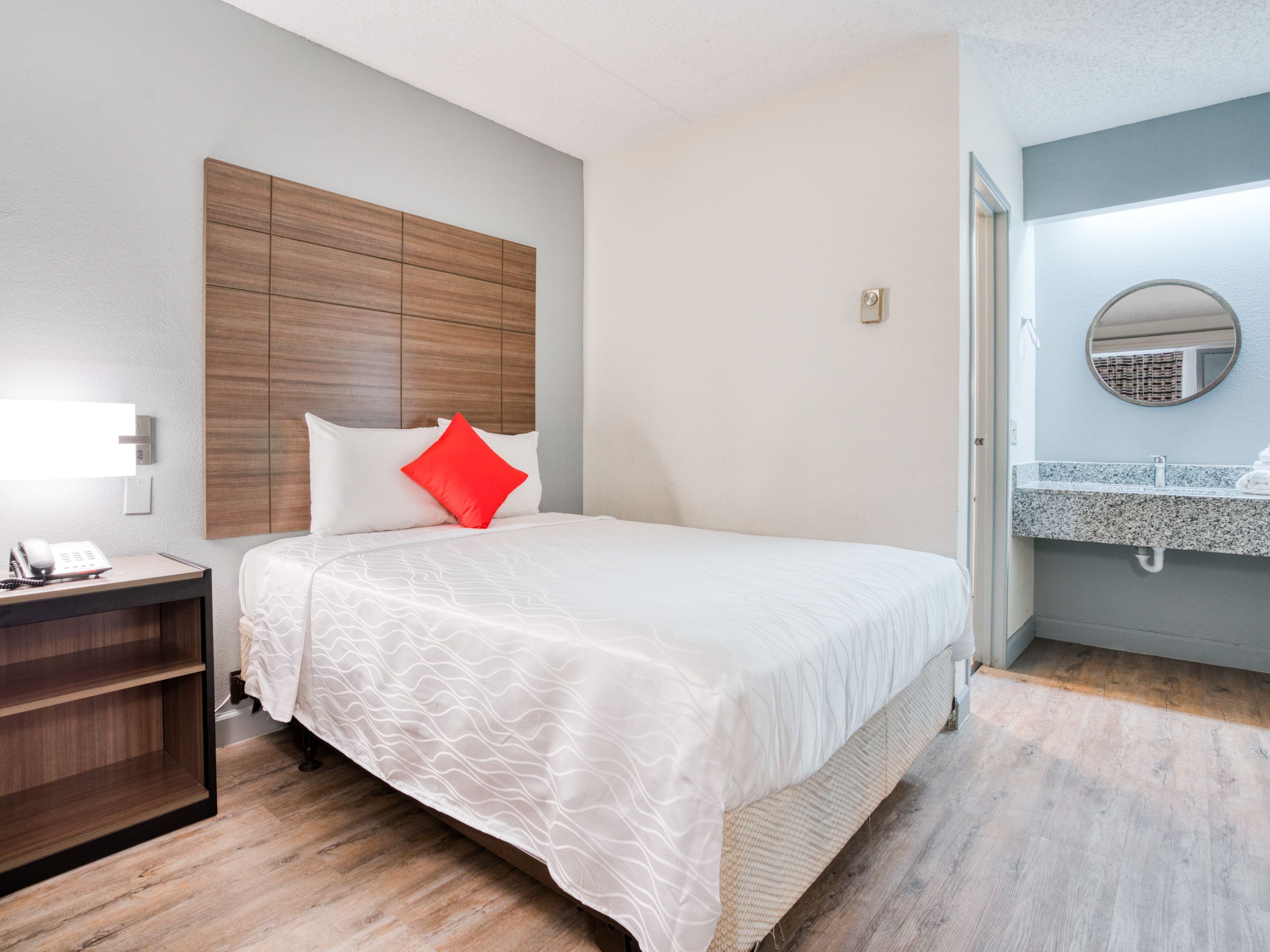 A hotel room with a bed, a nightstand, a telephone, and a bathroom with a sink and mirror.