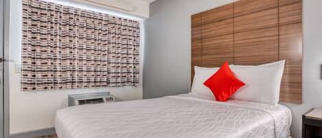 A neatly arranged hotel room with a bed, a window with striped curtains, a wooden headboard, and a small bedside table.