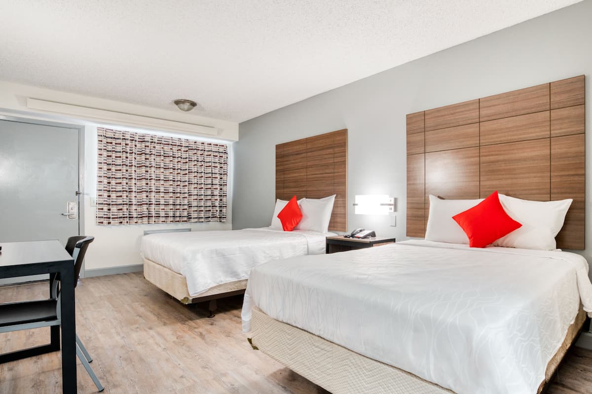 Quarto de hotel com duas camas, uma escrivaninha e uma janela com cortinas estampadas.