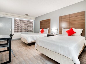 A hotel room with two beds, a desk, and a window with patterned curtains.