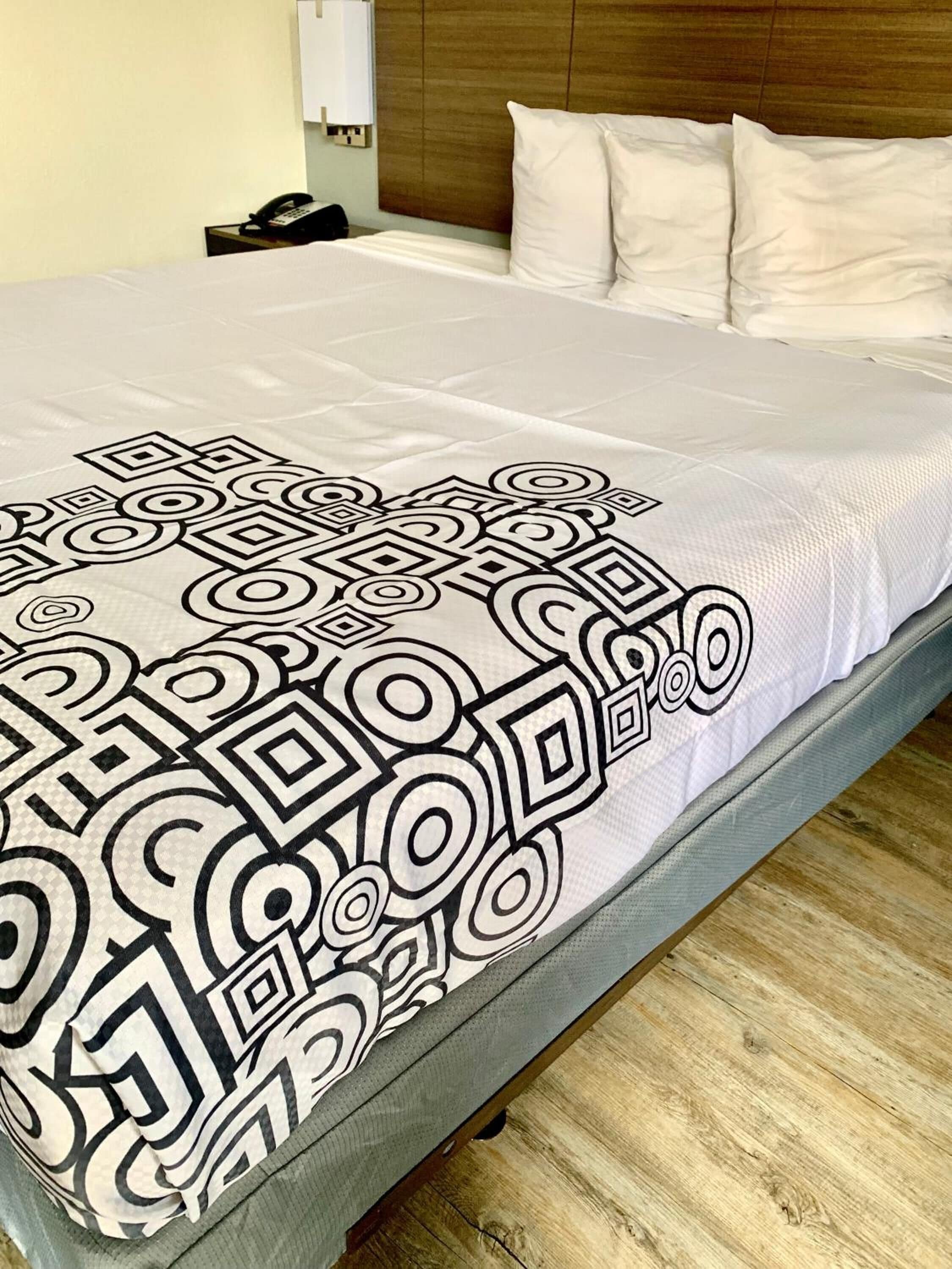 A bed with a patterned bedspread, a wooden headboard, and a bedside telephone.