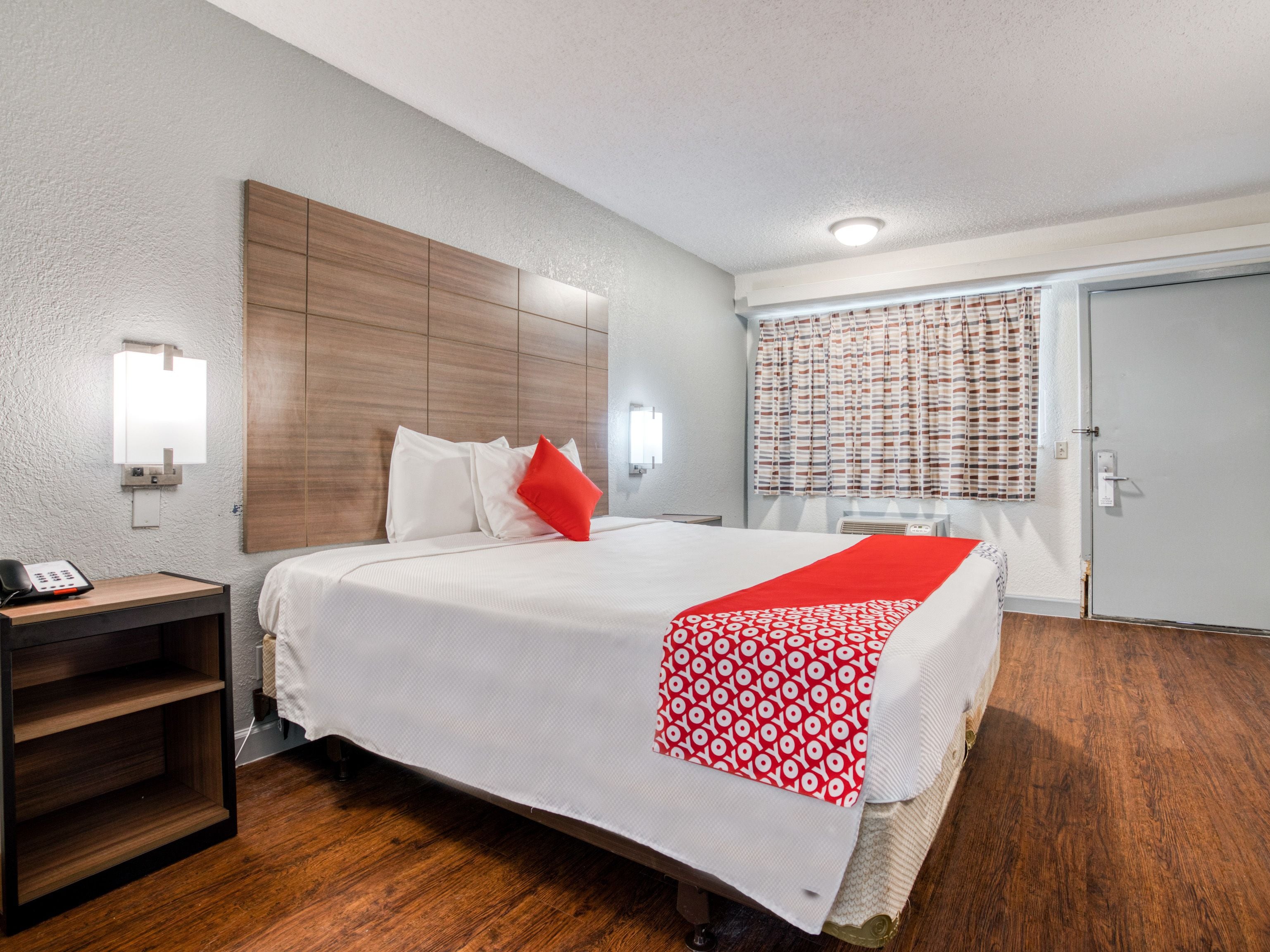 Habitación de hotel con cama, mesita de noche y escritorio con teléfono.