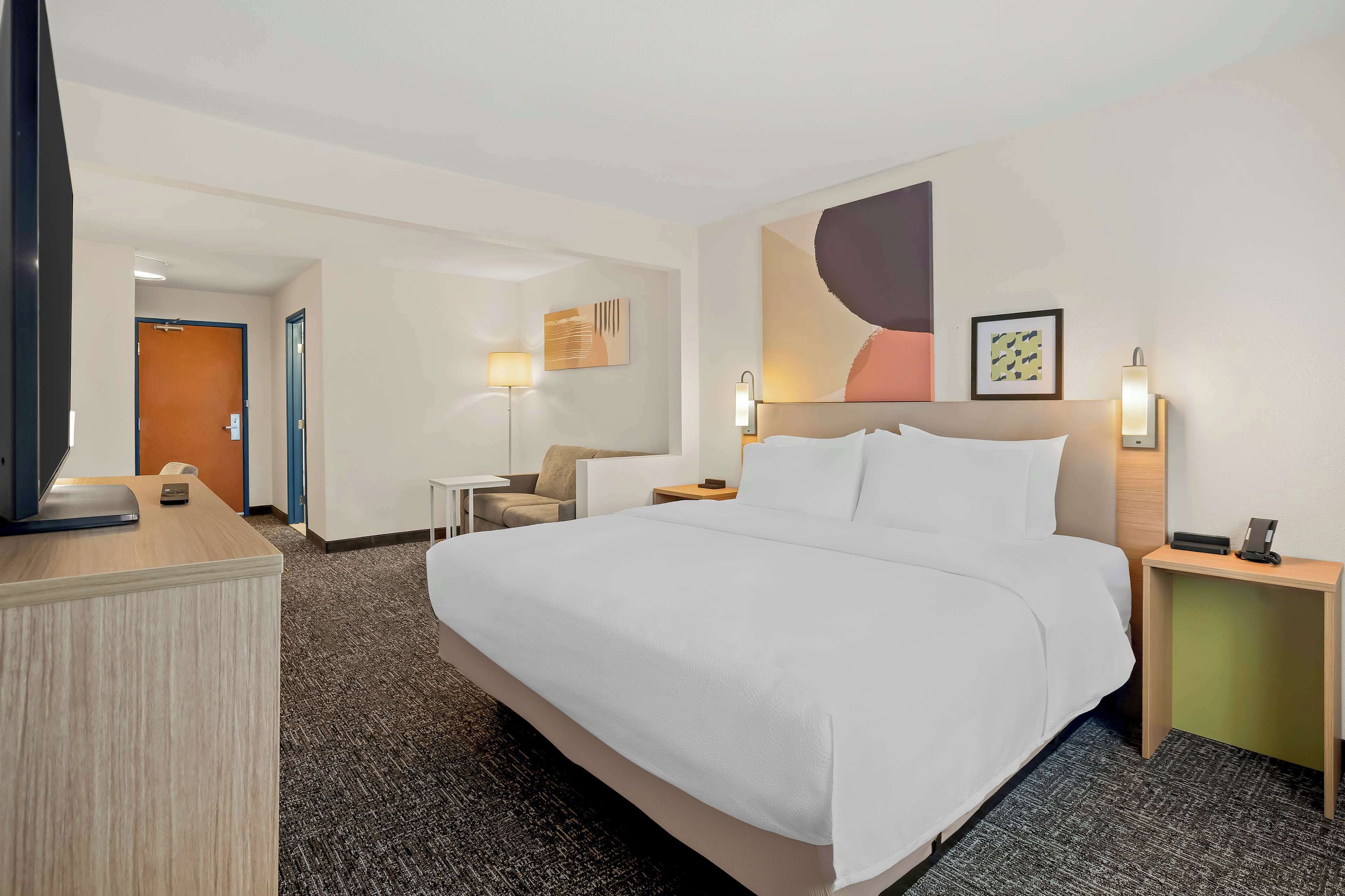 Una habitación de hotel con una cama grande, un escritorio, una silla, una lámpara y un cuadro en la pared.