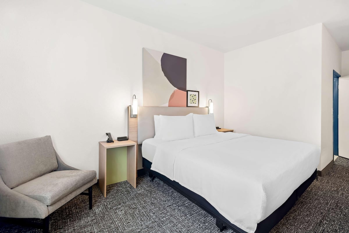 Una habitación de hotel con una cama, una silla, una mesita de noche y una obra de arte colgada en la pared.