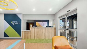 A hotel reception area with a modern design, including a reception desk, a seating area with a yellow chair, and a large window with a view of the outdoors. - Spark by Hilton Moline Quad Cities (Moline)