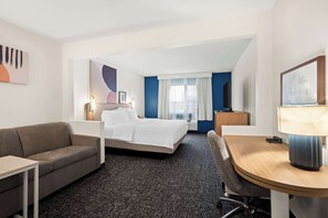 Una habitación de hotel con una cama, un escritorio, una silla, un sofá, una lámpara y un marco de fotos en la pared.