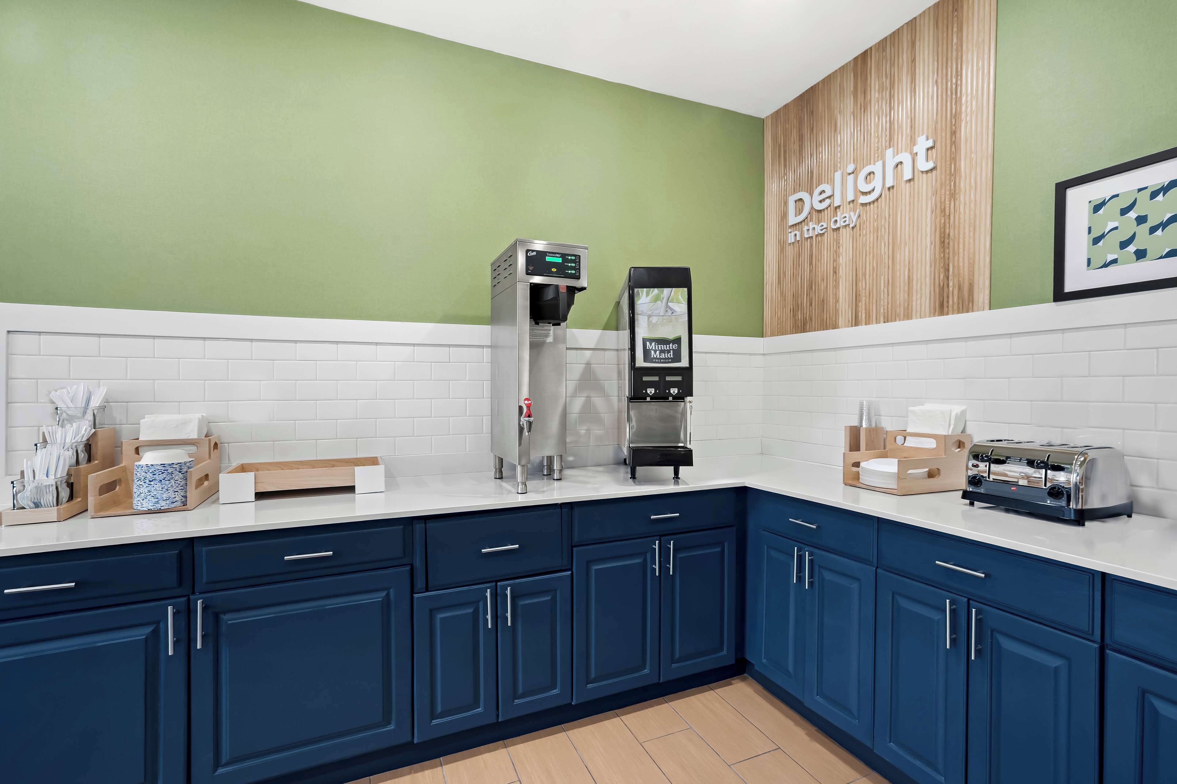 A modern kitchen with a coffee machine, toaster, and a wall-mounted sign that reads "delight in the day."