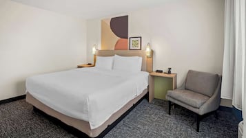 A hotel room with a large bed, a chair, a nightstand, and a wall-mounted artwork.