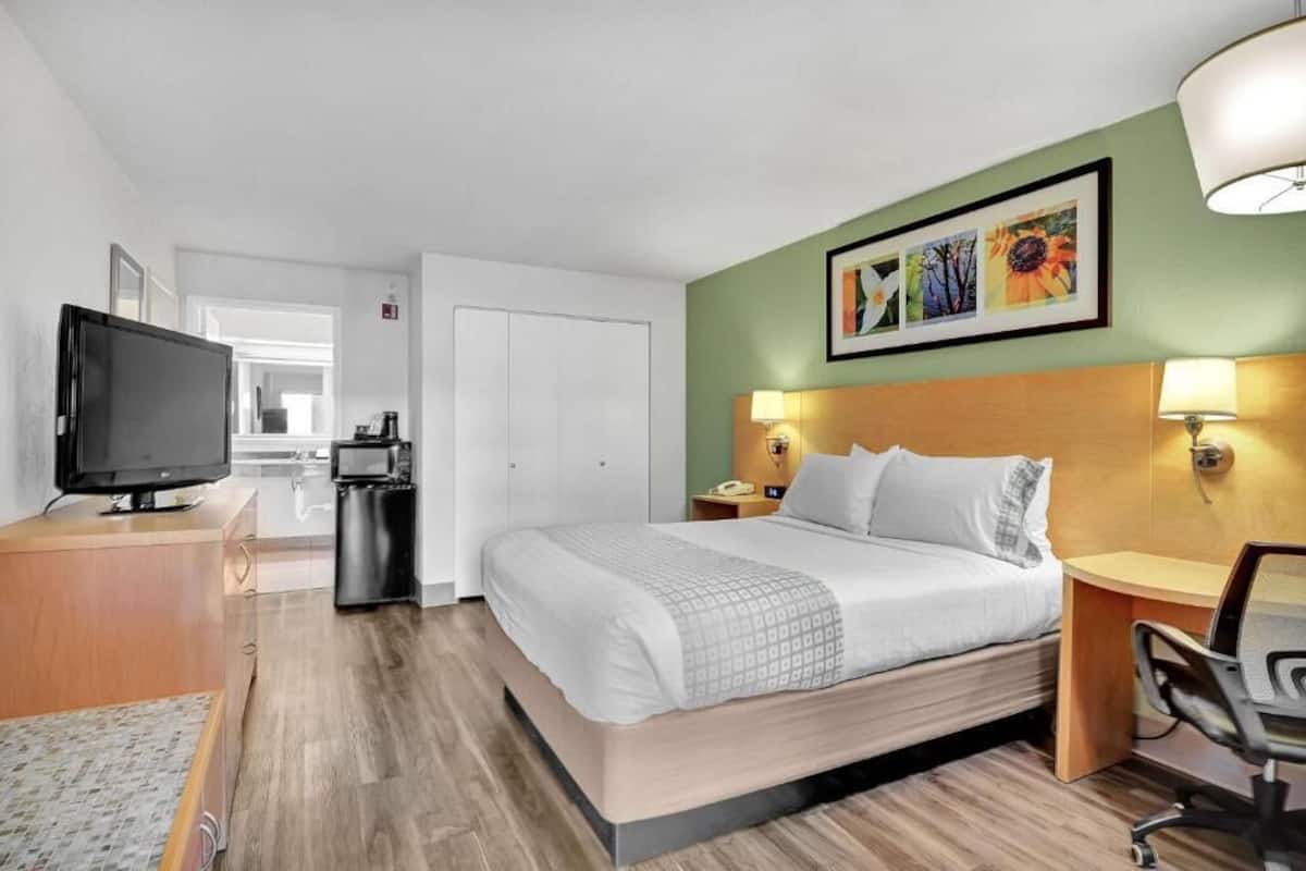 Ett hotellrum med en säng, sänglampor, ett skrivbord med en stol, en tv och en mikrovågsugn.