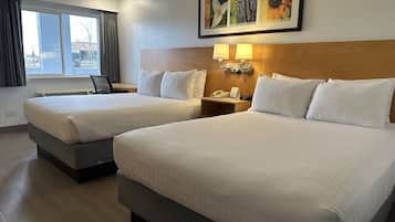 A hotel room with two beds, a nightstand with a lamp, a painting above the beds, and a window with curtains.