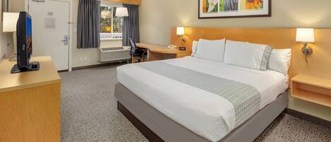 Une chambre d’hôtel avec un grand lit, un bureau avec un ordinateur, une télévision et une fenêtre avec des rideaux.