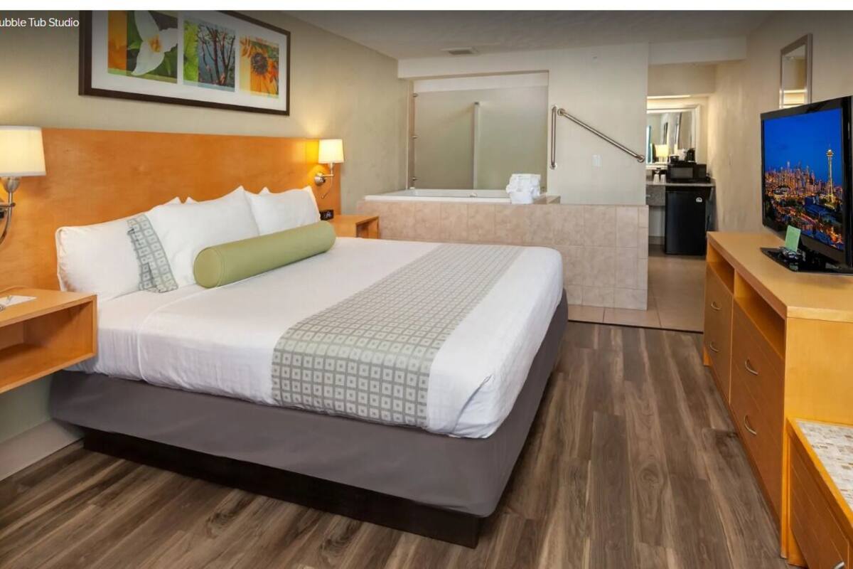 Ett hotellrum med en säng, en tv, ett skrivbord, en spegel och ett badrum som syns genom en öppen dörr.