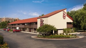 A Red Roof Inn with a red roof and beige walls, parking lot, and surrounding greenery. - Red Roof Inn Detroit - Dearborn/Greenfield Village (Dearborn)