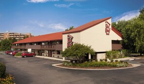 A Red Roof Inn with a red roof and beige walls, parking lot, and surrounding greenery. - Red Roof Inn Detroit - Dearborn/Greenfield Village (Dearborn)