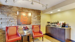 A Red Roof Inn reception area with two leather chairs, a small table with a vase of flowers, and a kitchen area with a coffee station. - Red Roof Inn Detroit - Dearborn/Greenfield Village (Dearborn)