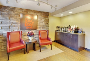 A Red Roof Inn reception area with two leather chairs, a small table with a vase of flowers, and a kitchen area with a coffee station. - Red Roof Inn Detroit - Dearborn/Greenfield Village (Dearborn)