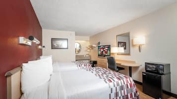A hotel room with two beds, a desk, a chair, a microwave, and a small refrigerator.