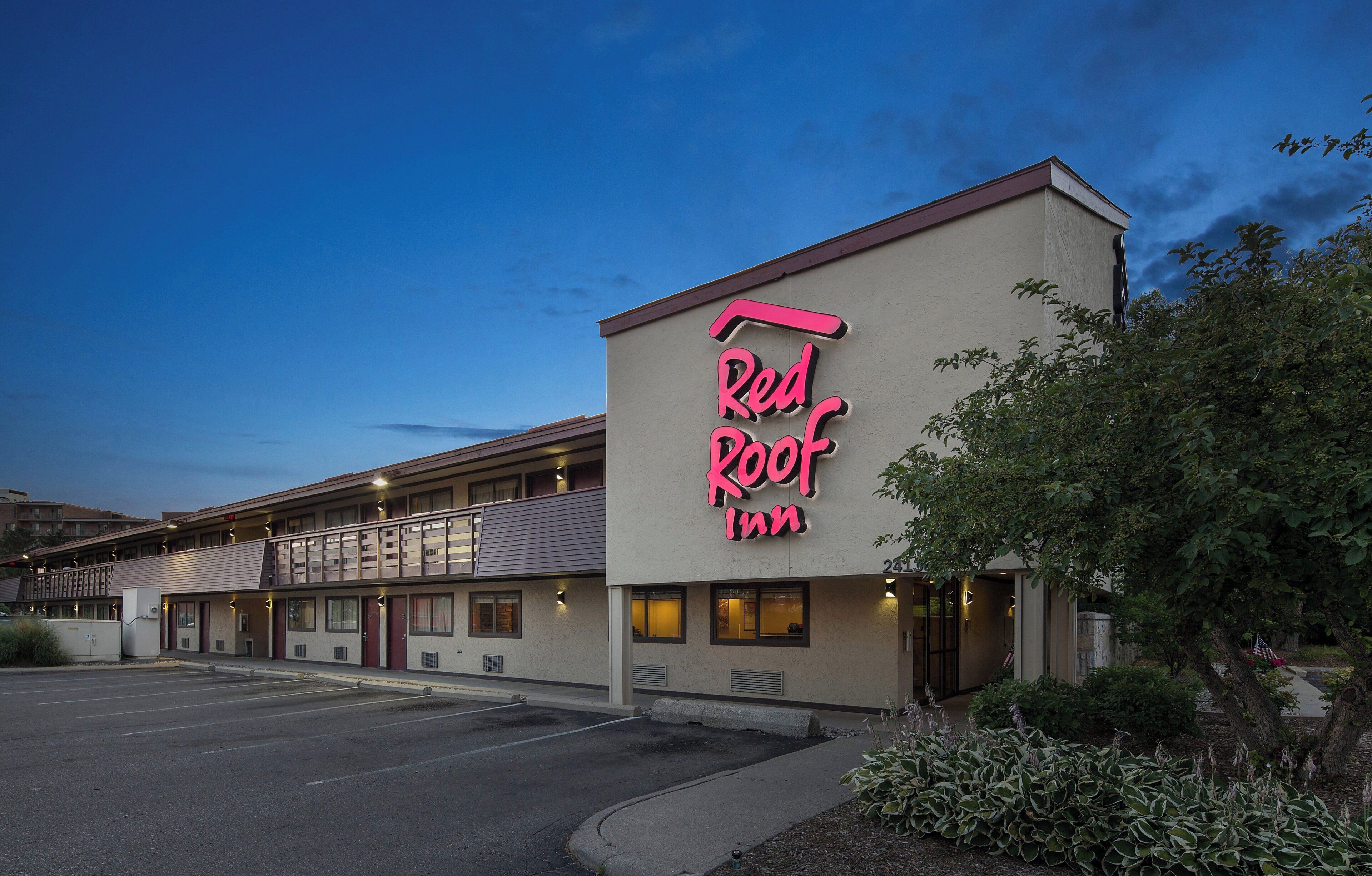 A Red Roof Inn with a neon sign, a parking lot, and a building with multiple windows and a flat roof.