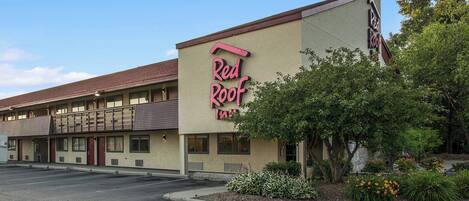 A Red Roof Inn with a two-story building, a parking lot, and landscaped areas with shrubs and flowers.
