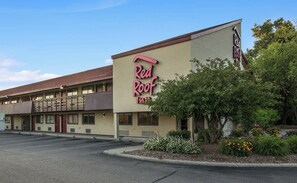 A Red Roof Inn with a two-story building, a parking lot, and landscaped areas with shrubs and flowers.