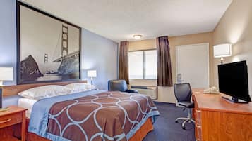 A hotel room with a large bed, a desk with a computer, a TV, and a window with curtains.