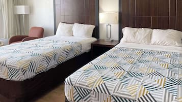 Dos camas dobles con ropa de cama estampada, una mesita de noche con lámpara y una silla en una habitación de hotel.