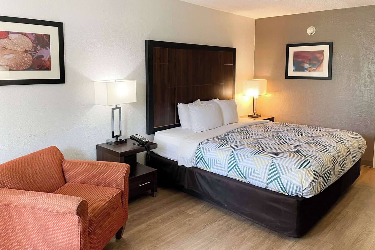 A hotel room with a bed, two bedside tables with lamps, a chair, and two framed pictures on the walls.