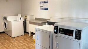 Una sala de lavandería con lavadora de carga frontal, secadora de carga superior y una mesa para doblar ropa.