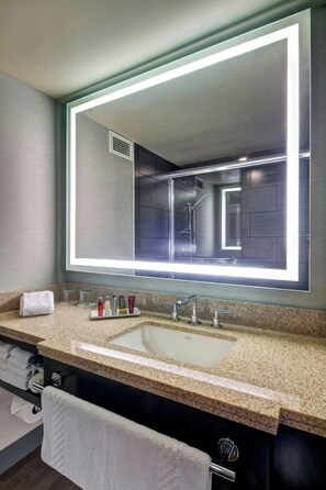 A modern bathroom with a large mirror, granite countertop, and a white sink.