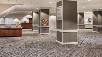 A hotel lobby with a reception desk, a decorative geometric sculpture, and a carpet with a herringbone pattern.