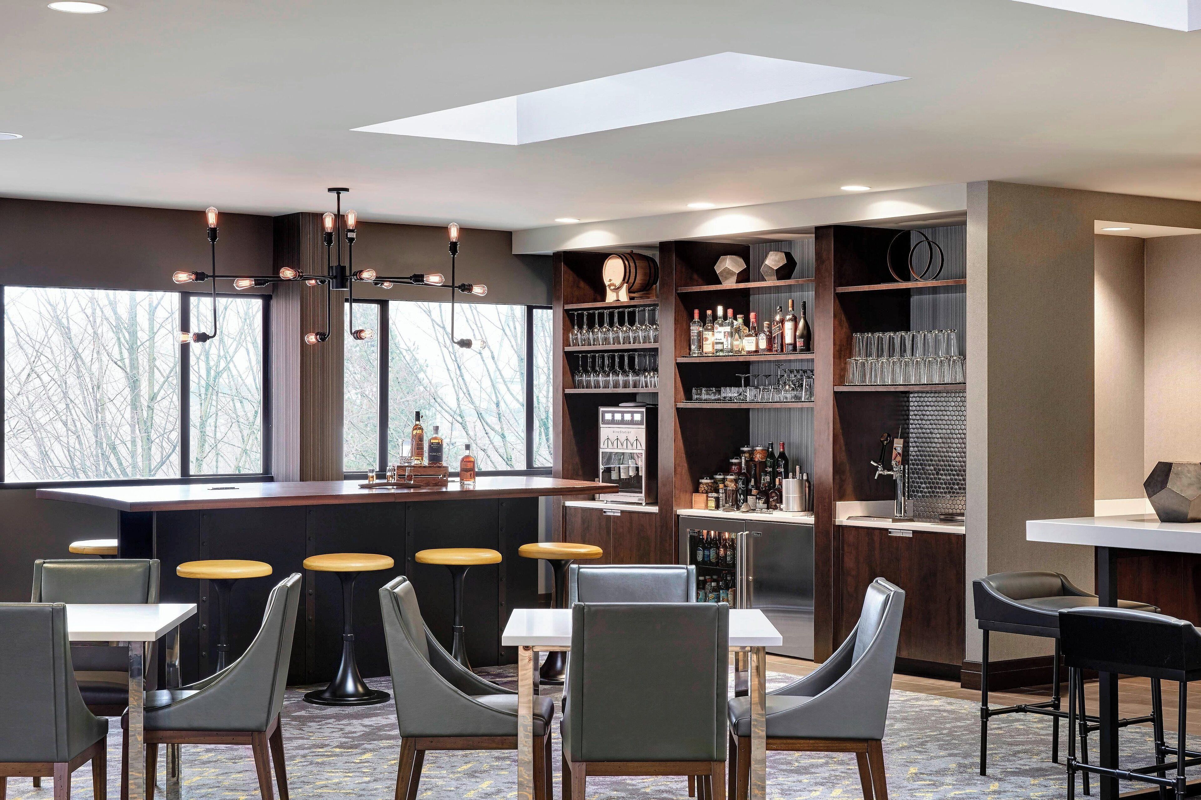 A modern bar area with seating, a bar counter, and shelves stocked with bottles and glasses.