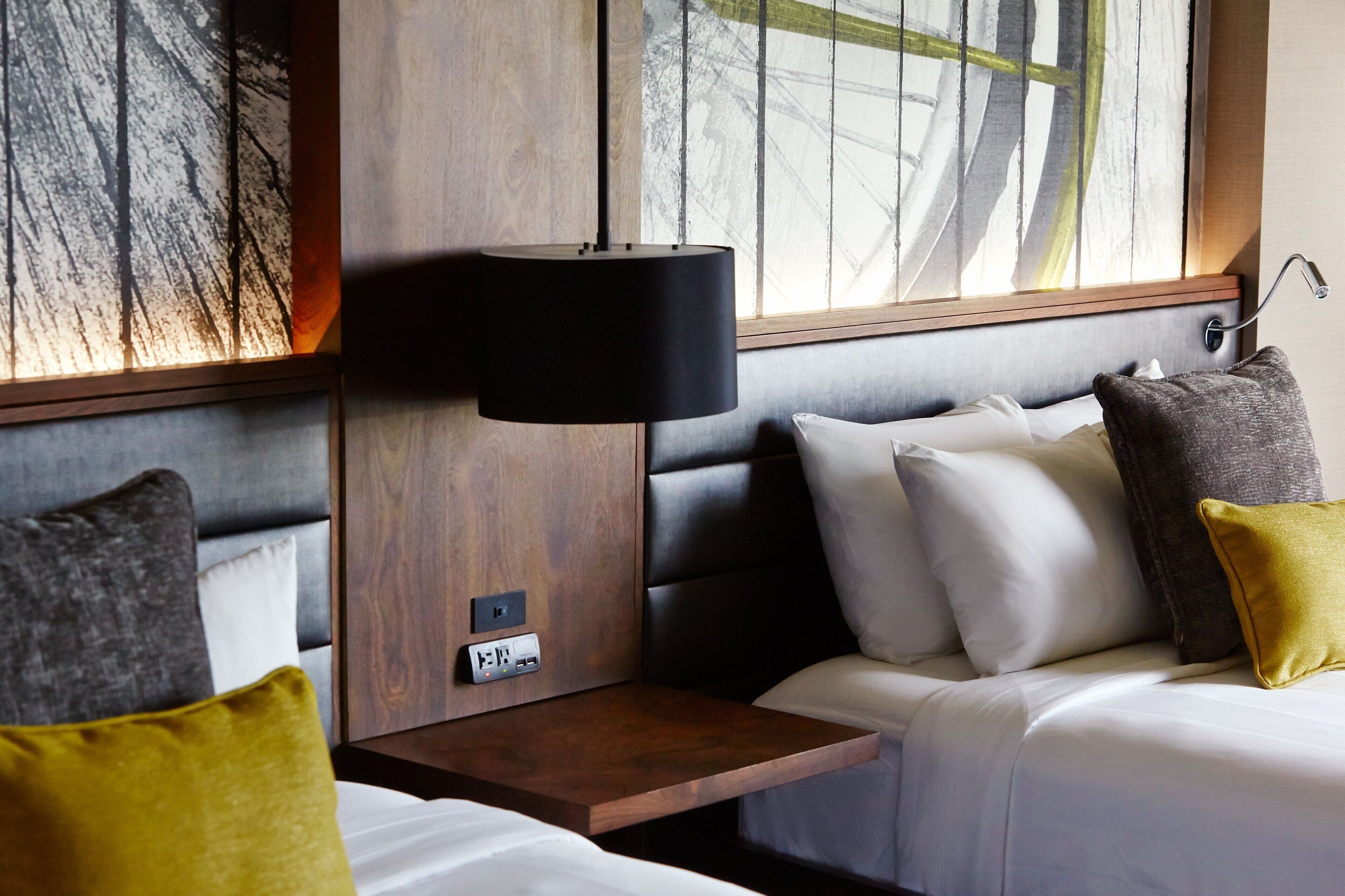 A hotel room with a bed, bedside table, lamp, and artwork on the wall.