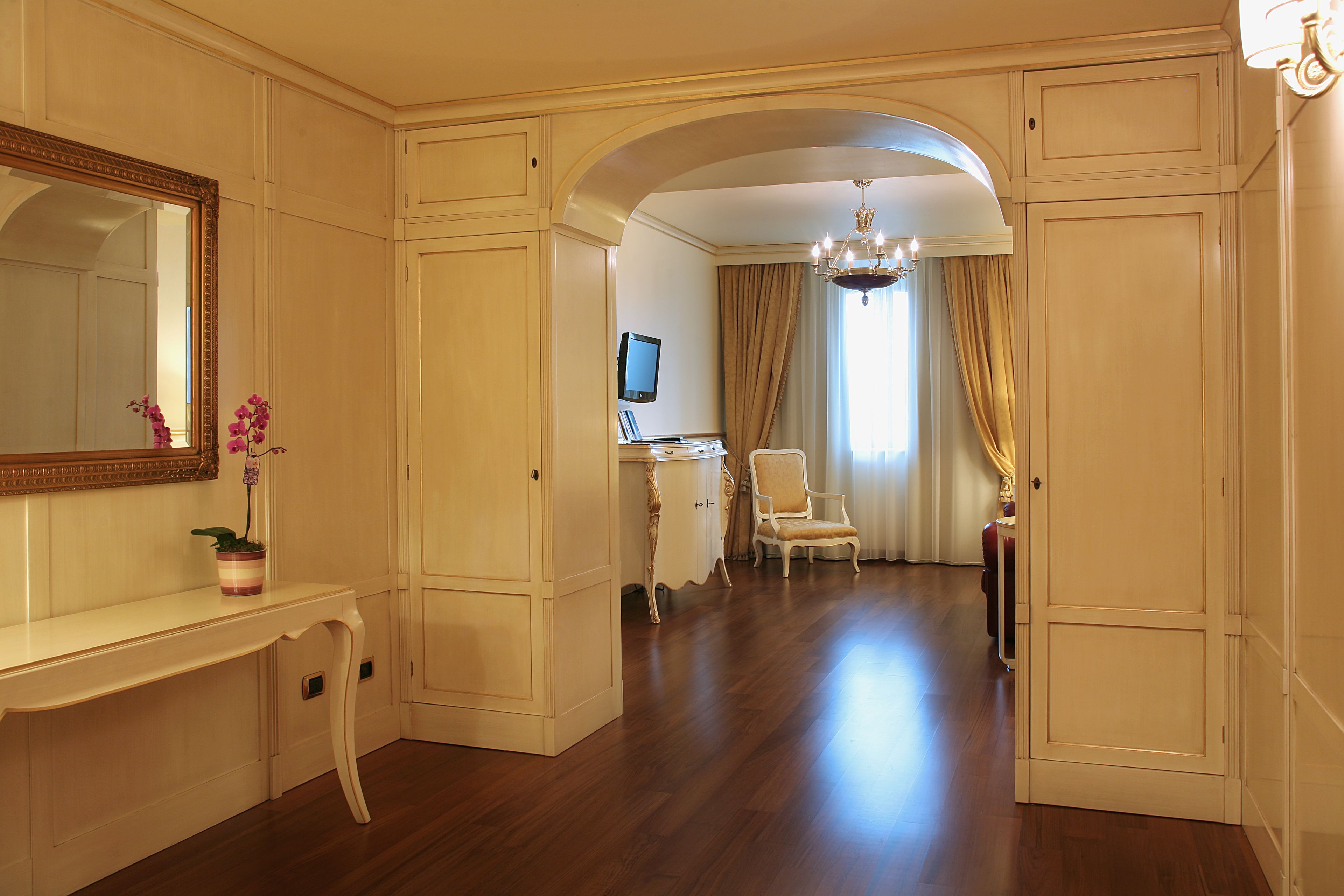 A room with a large mirror, a vanity with a television, a chair, and a chandelier.