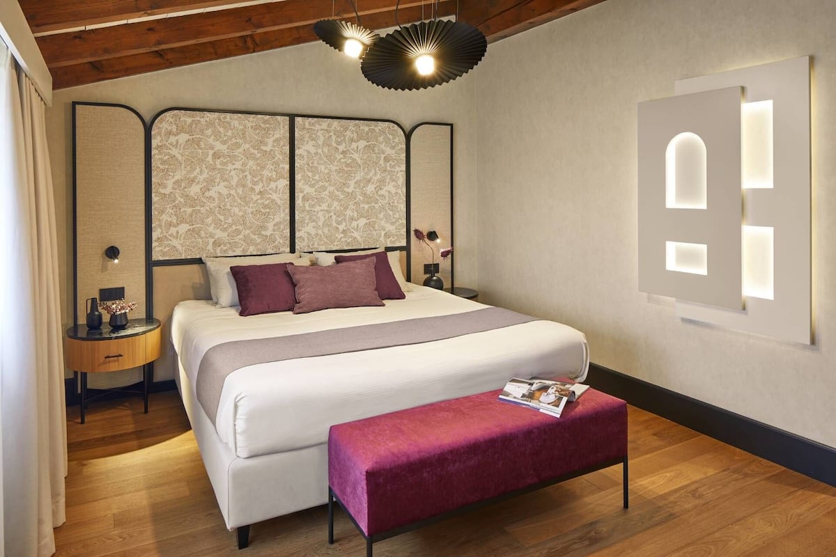 Une chambre moderne avec un grand lit, une table de chevet, un banc et un décor mural original.
