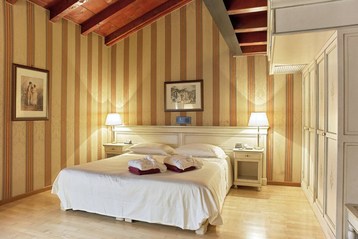 Une chambre d’hôtel avec un grand lit, deux tables de chevet, une petite table et une armoire.