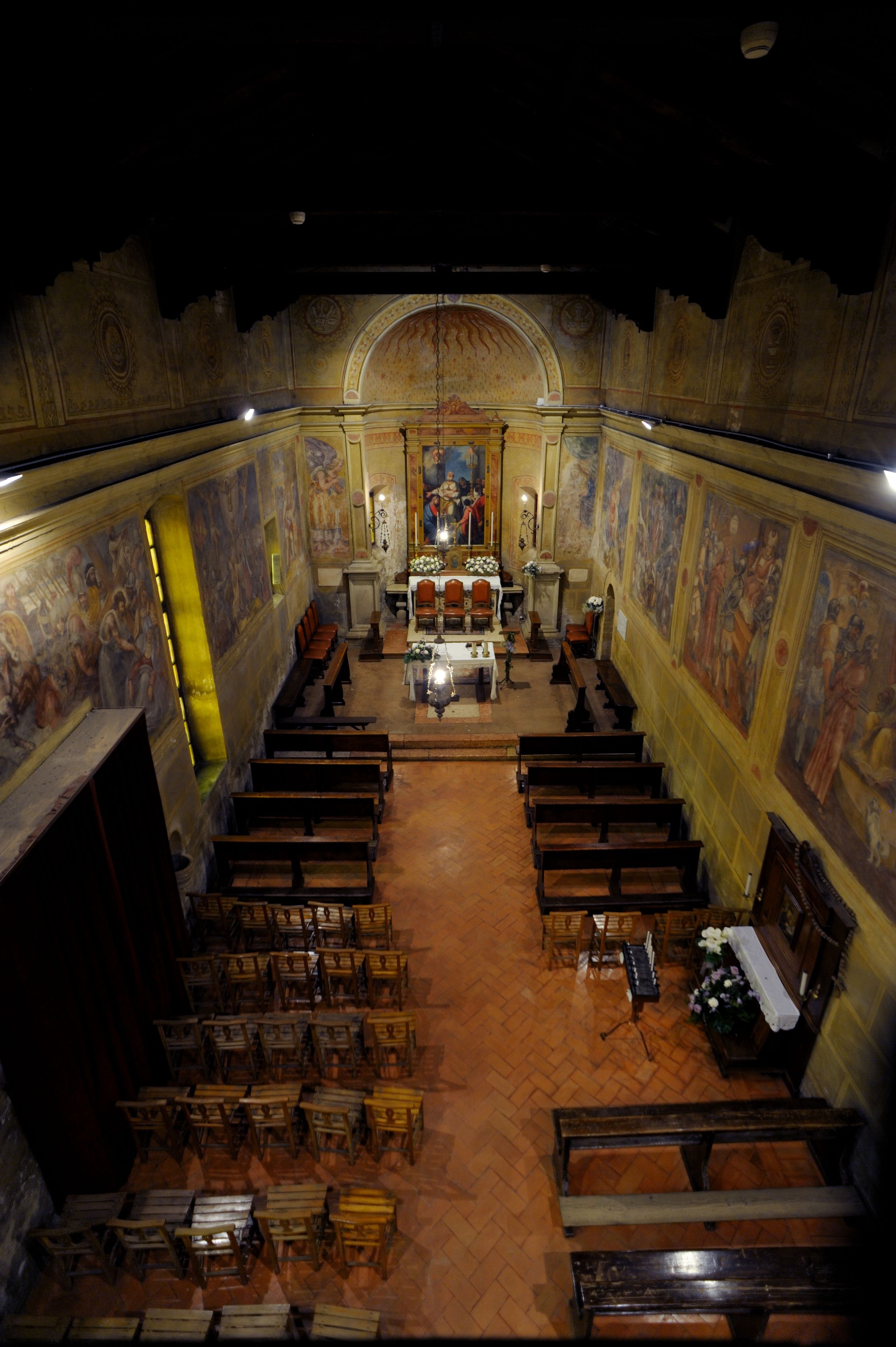 L’intérieur d’une église, avec des rangées de bancs en bois, un autel central et des fresques détaillées sur les murs.