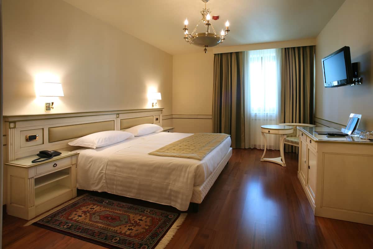 Une chambre d’hôtel avec un grand lit, des lampes de chevet, un bureau avec un ordinateur, une télévision et un lustre.