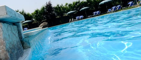 A swimming pool with clear water, surrounded by lounge chairs and umbrellas.