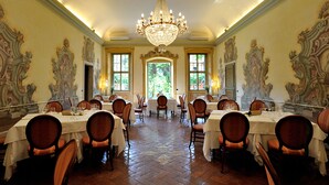 A formal dining room with ornate wall decorations, a chandelier, and multiple tables set for dining.